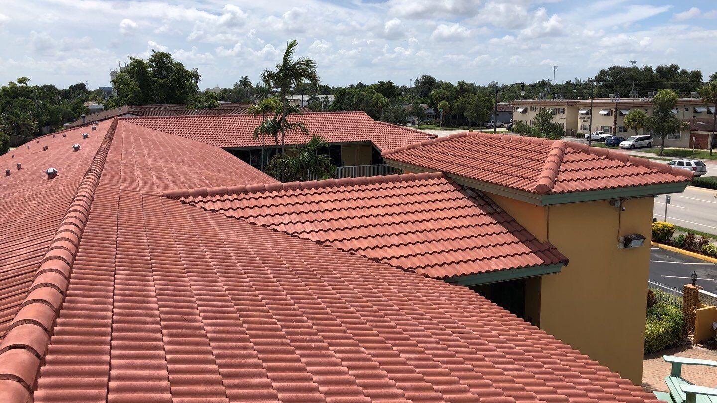 Red tile roof of a building with a courtyard, surrounded by trees and a sunny sky.