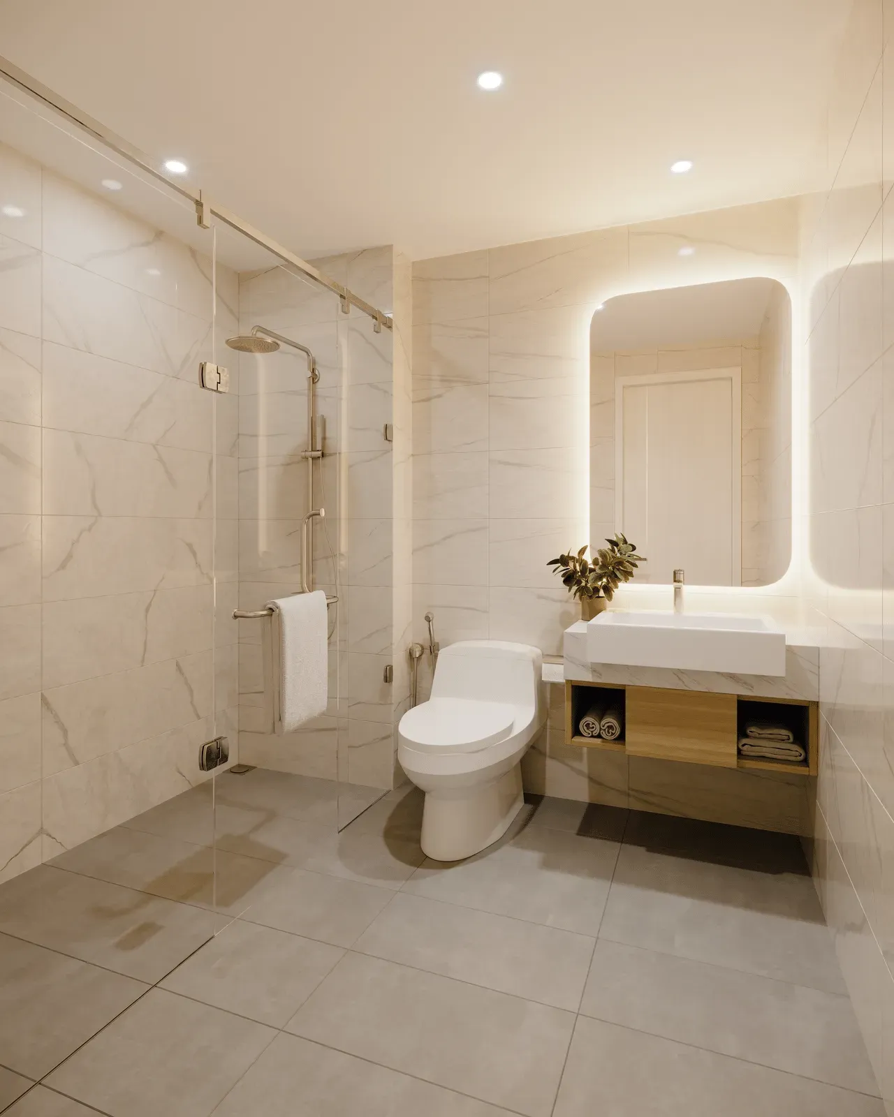 Modern bathroom with white marble walls, glass shower, toilet, and vanity with a lighted mirror.