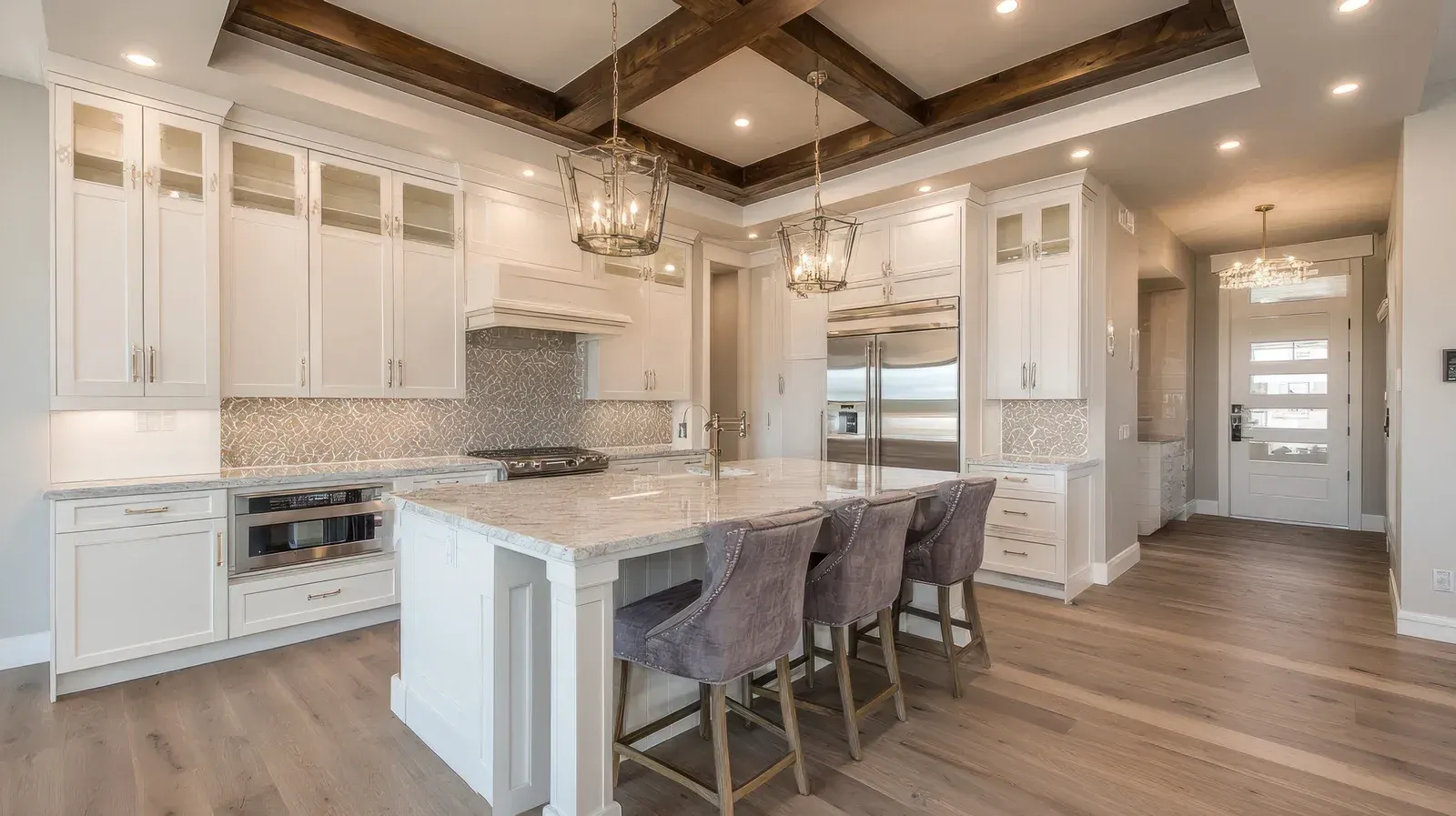 Elegant white kitchen with island, wooden beams, stainless steel appliances, and hardwood floors.