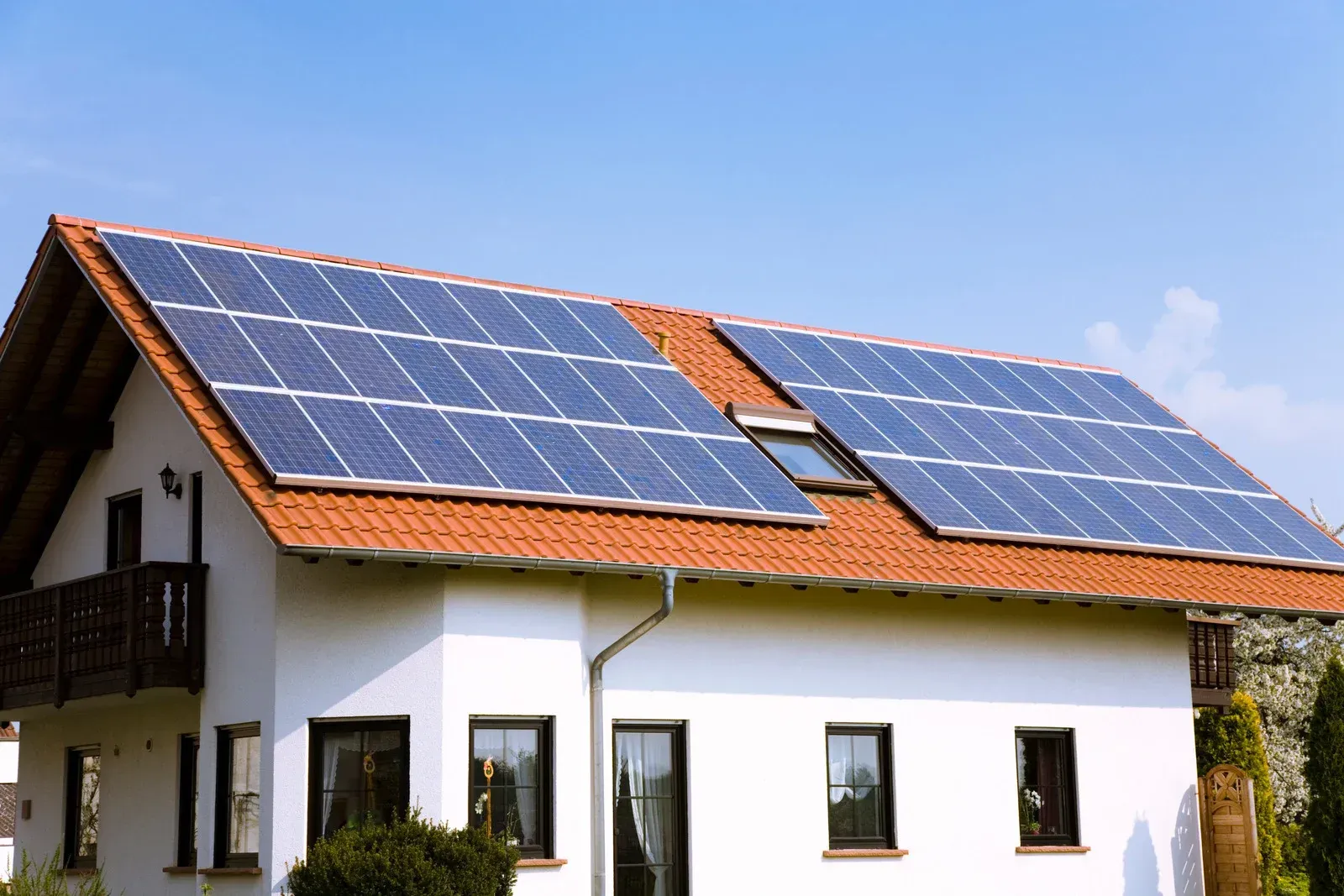 White house with red tile roof and solar panels, blue sky.