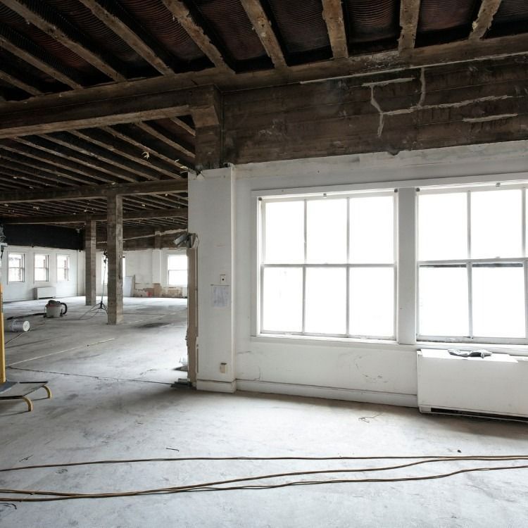 Interior of a large, unfinished room with exposed wooden beams, white walls, and large windows.