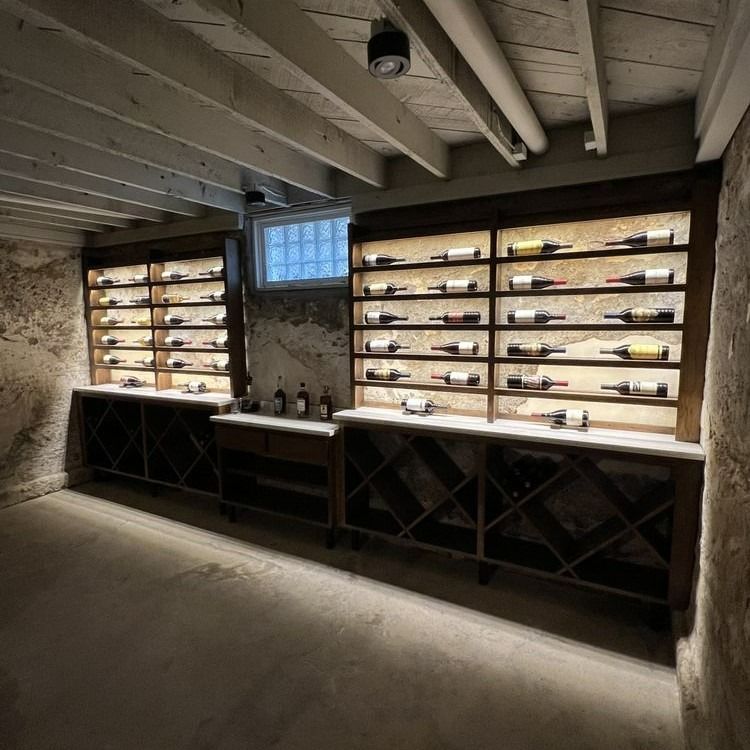 Basement wine cellar with wooden shelves, backlit bottles, and storage racks below.