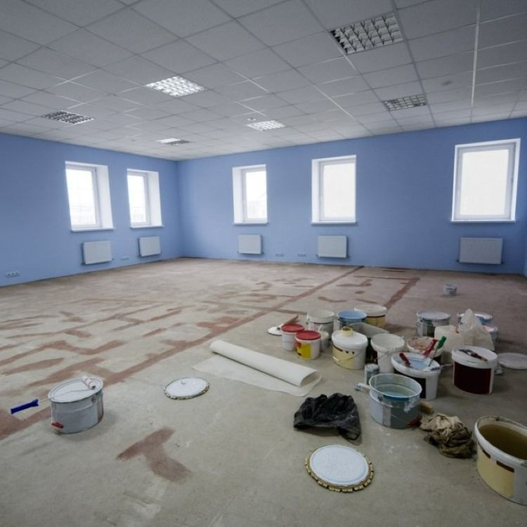 Empty room with blue walls, white ceiling, windows, and paint supplies on the floor.
