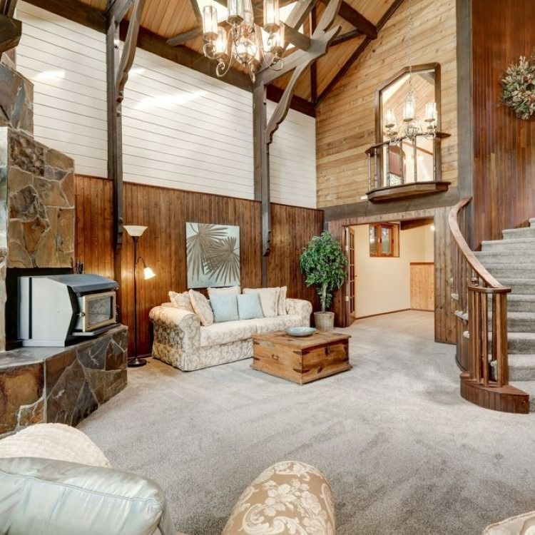 Living room with stone fireplace, wooden beams, carpet, and staircase.