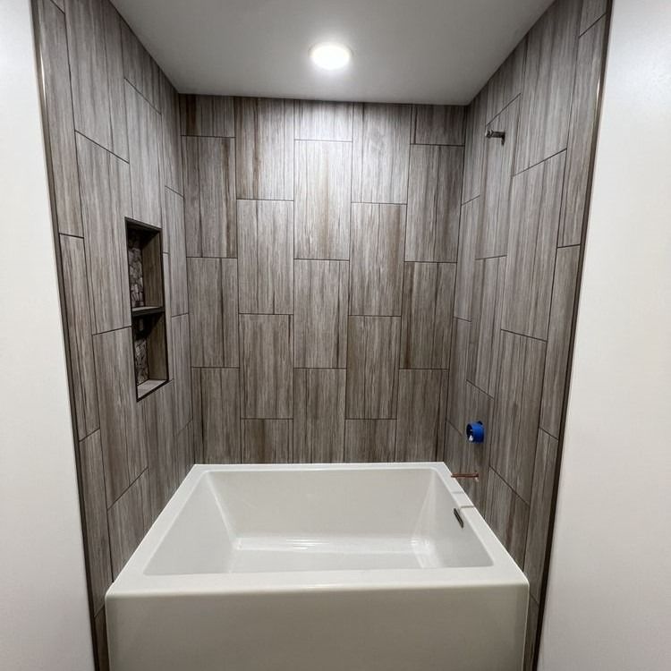 Bathroom with a white square tub, tiled walls in a wood grain pattern, recessed shelf.