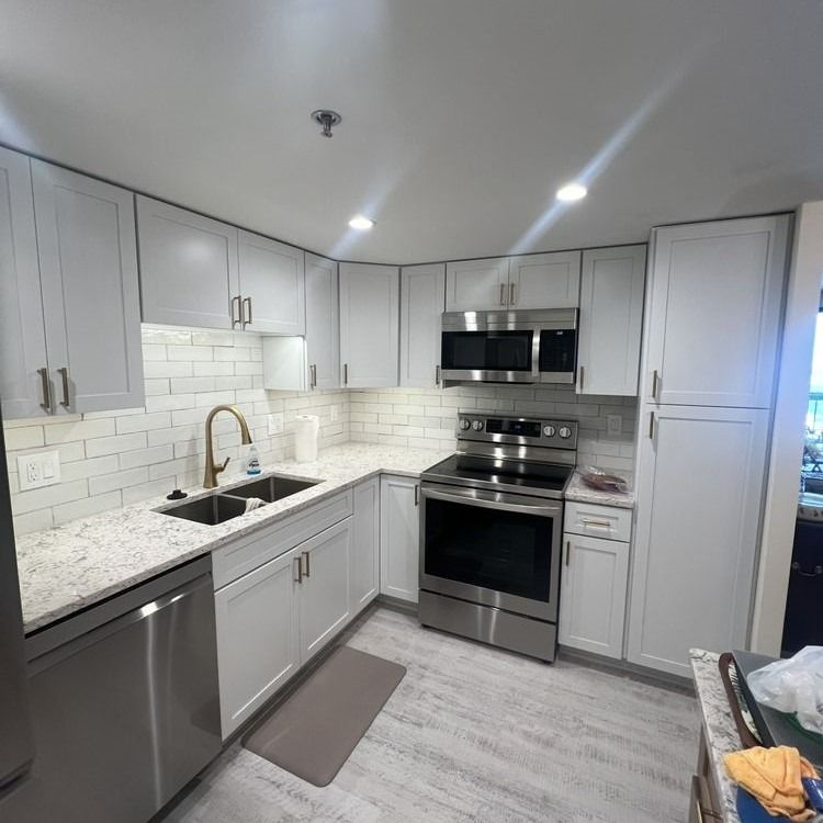 Modern kitchen with light gray cabinets, stainless steel appliances, and white tile backsplash.