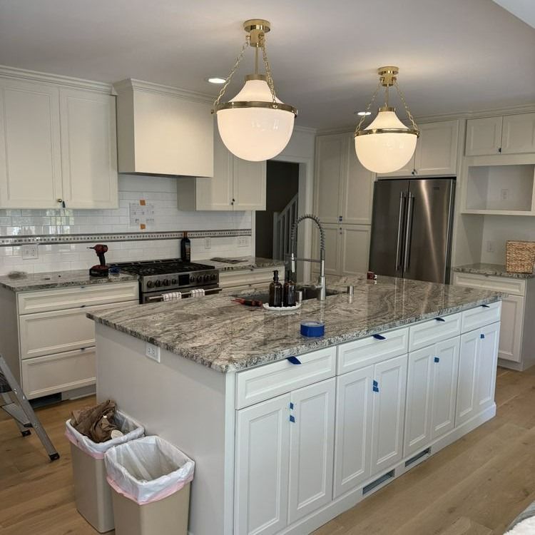 White kitchen with granite countertops, island with pendant lights, stainless steel refrigerator.