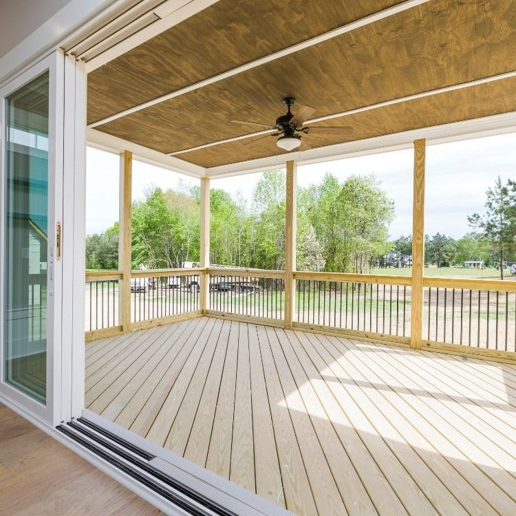 Wooden porch with a ceiling fan, sliding door, and a view of trees.