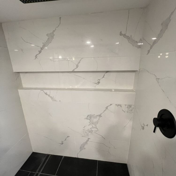 White marble tiled shower with recessed shelves, black fixtures, and black floor tiles.