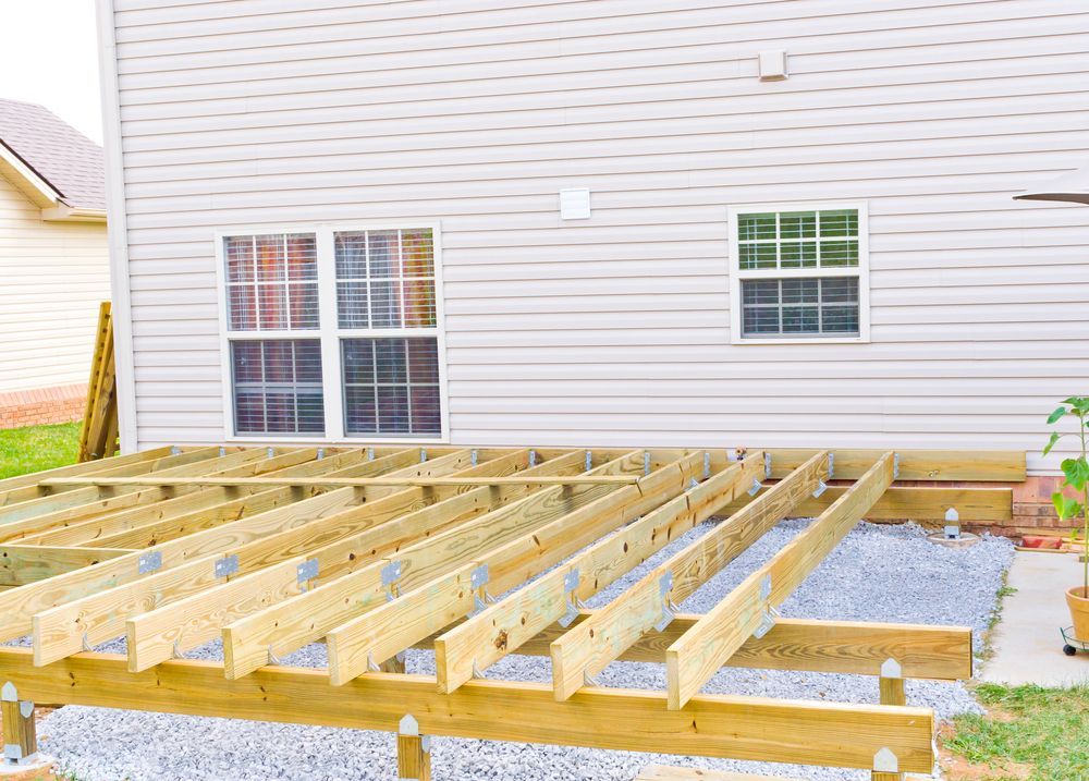 Wooden deck frame under construction against a beige house with windows.