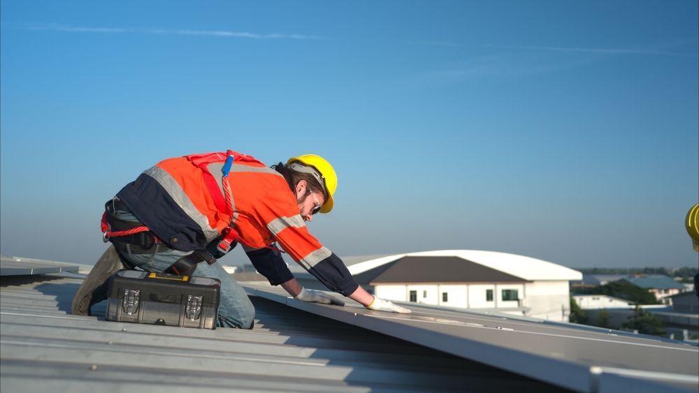 Rooftop worker in safety gear installing solar panels on a sunny day.