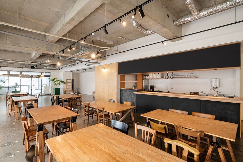 A light-filled cafe with wooden tables and chairs, a black counter, and a concrete ceiling.
