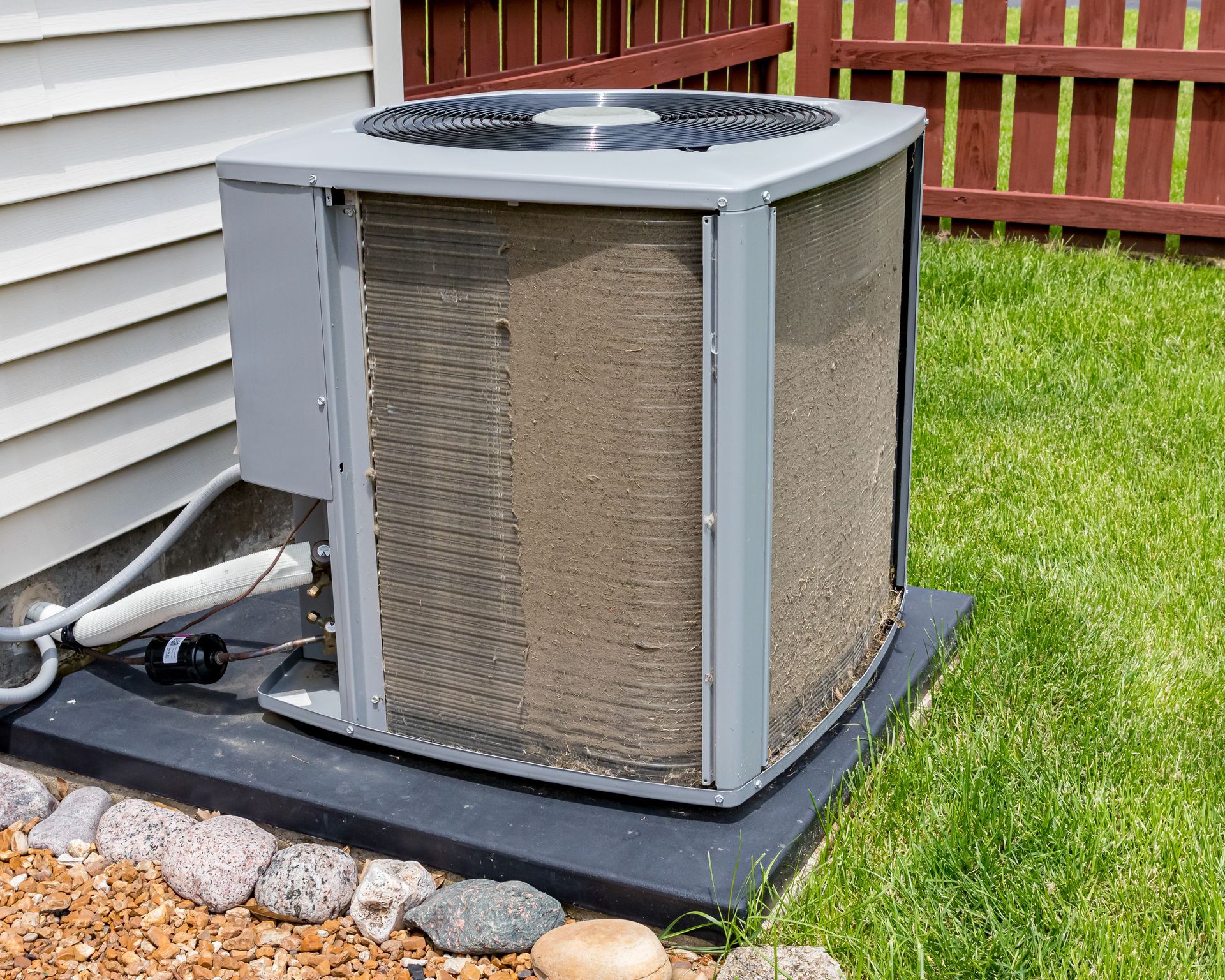 A gray residential outdoor air conditioning unit with heavily clogged, dirty condenser coils, sitting on a pad.