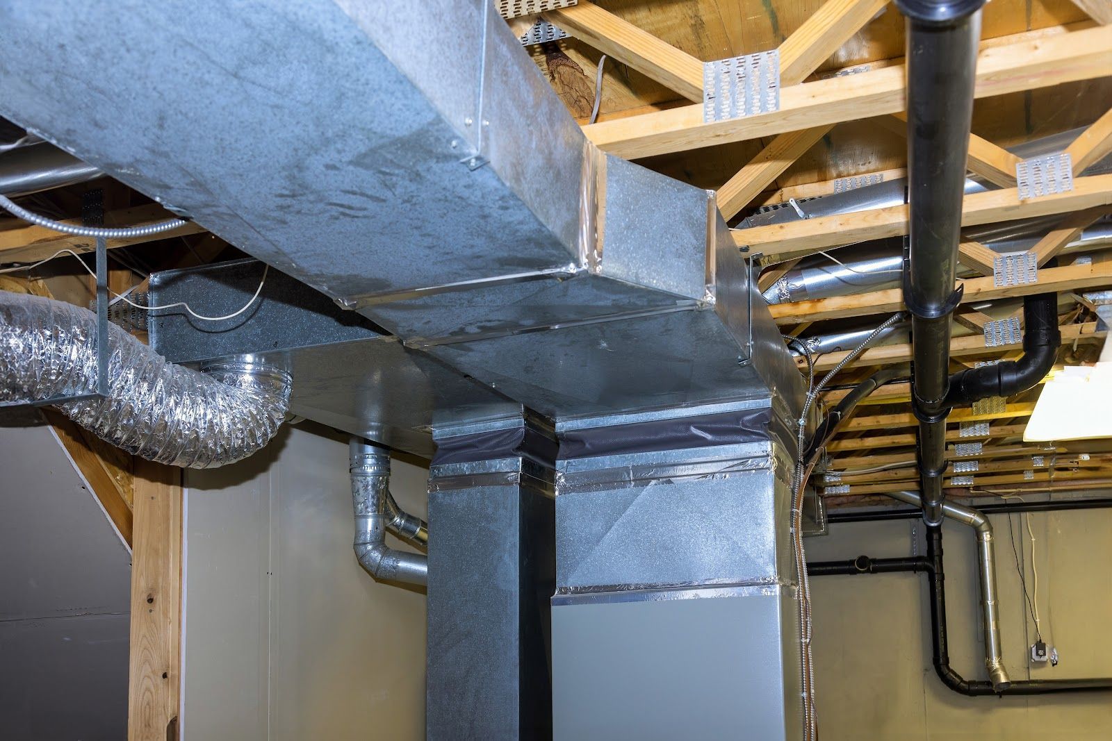 Galvanized metal HVAC ductwork and pipes installed in a basement ceiling.