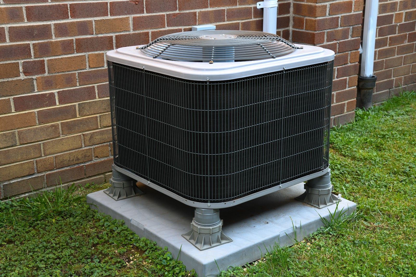 Air conditioning unit on a concrete pad near a brick wall.