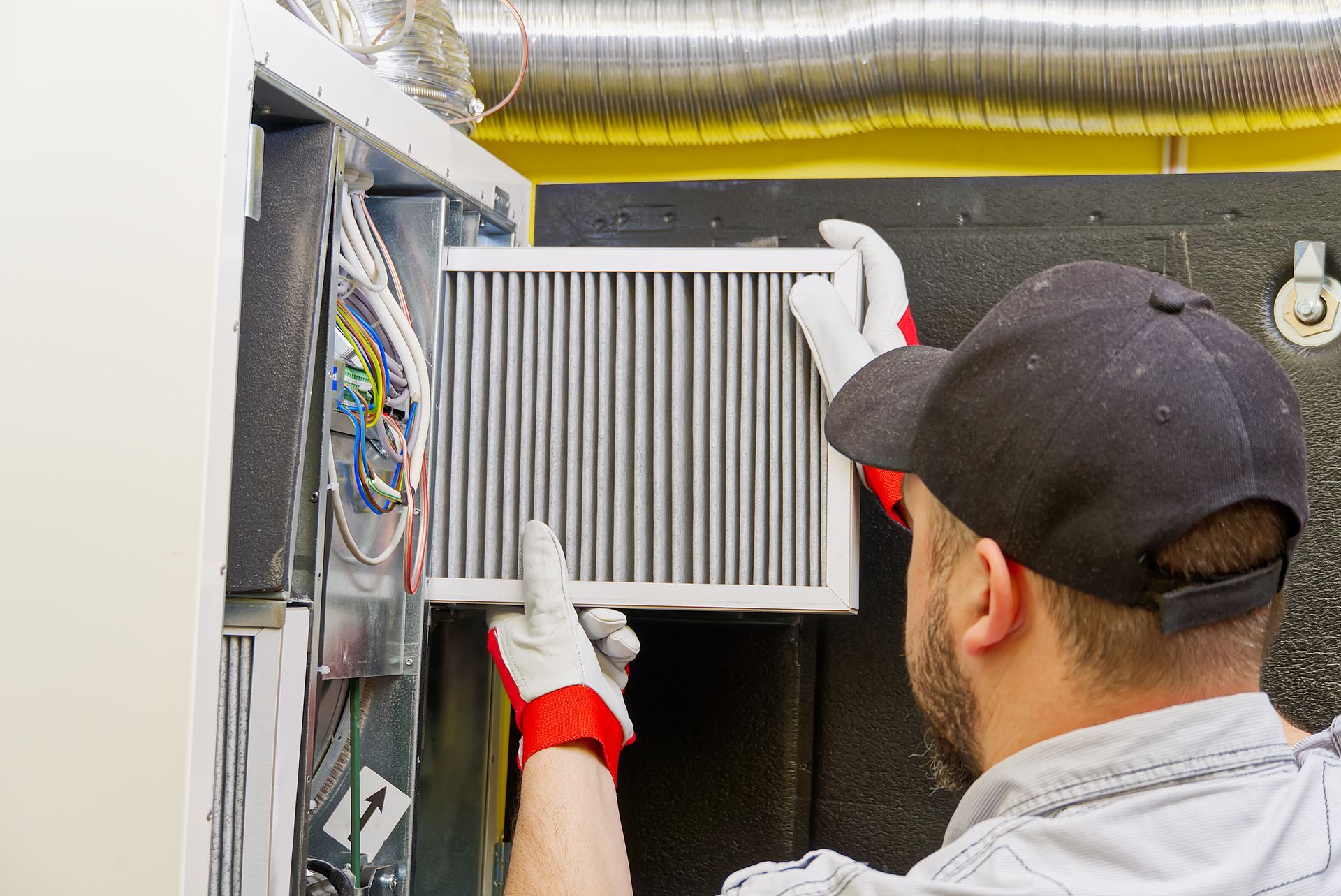 A worker wearing gloves and a cap slides a clean air filter into an HVAC system unit.