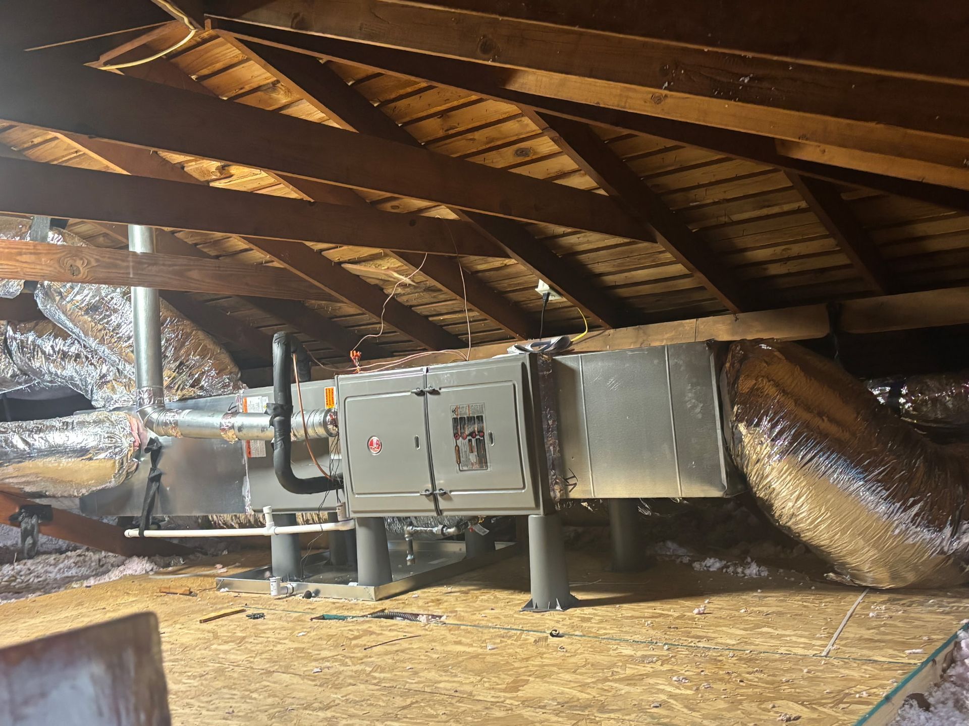 HVAC unit in an attic. Ductwork, insulation, and wooden beams are visible.