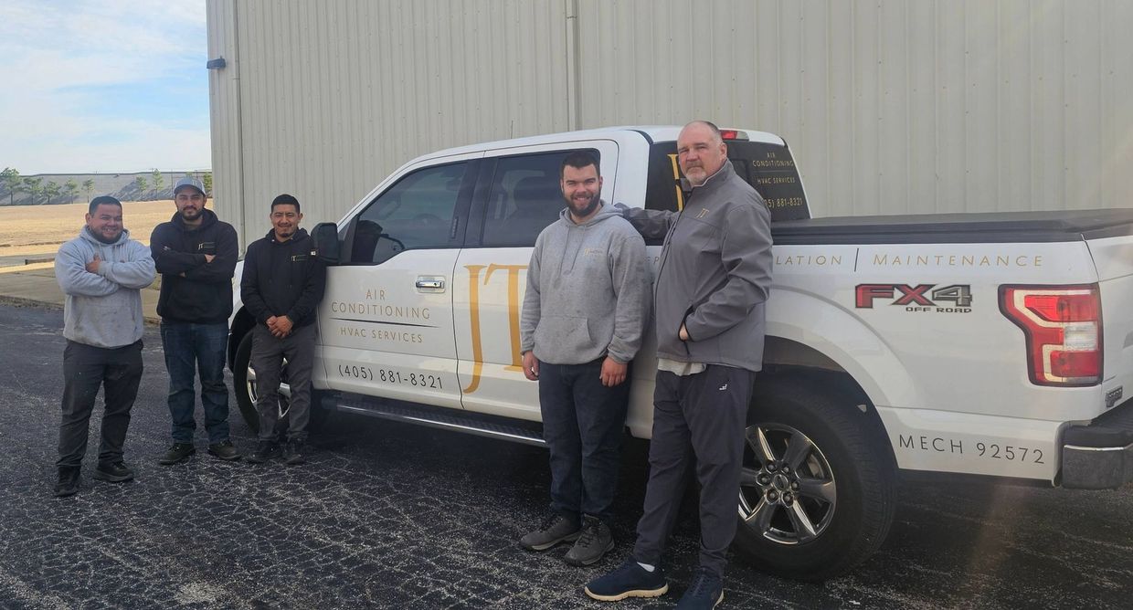 Five men stand next to a white pickup truck in an outdoor setting. The men have various expressions.