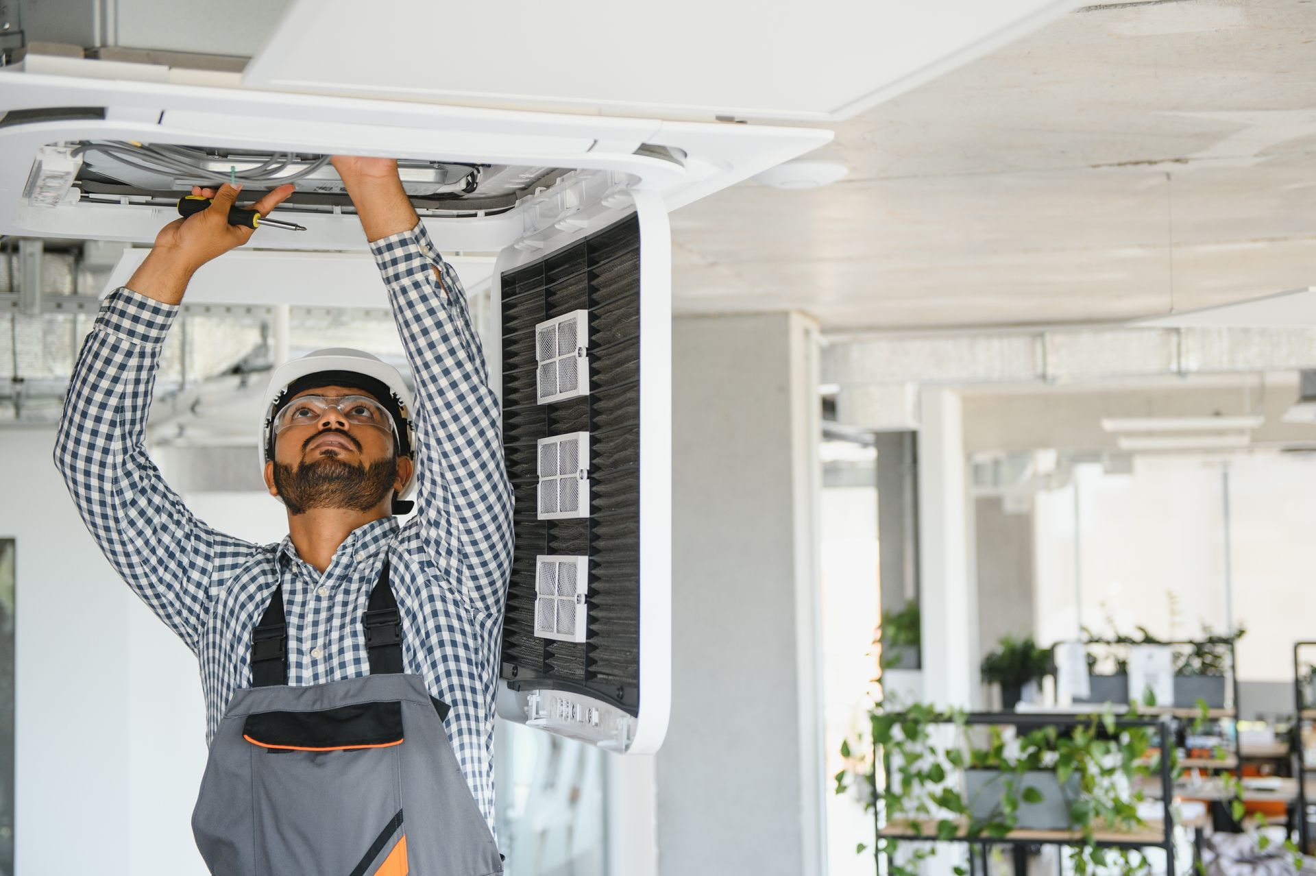 Person in overalls repairing a ceiling air conditioning unit.
