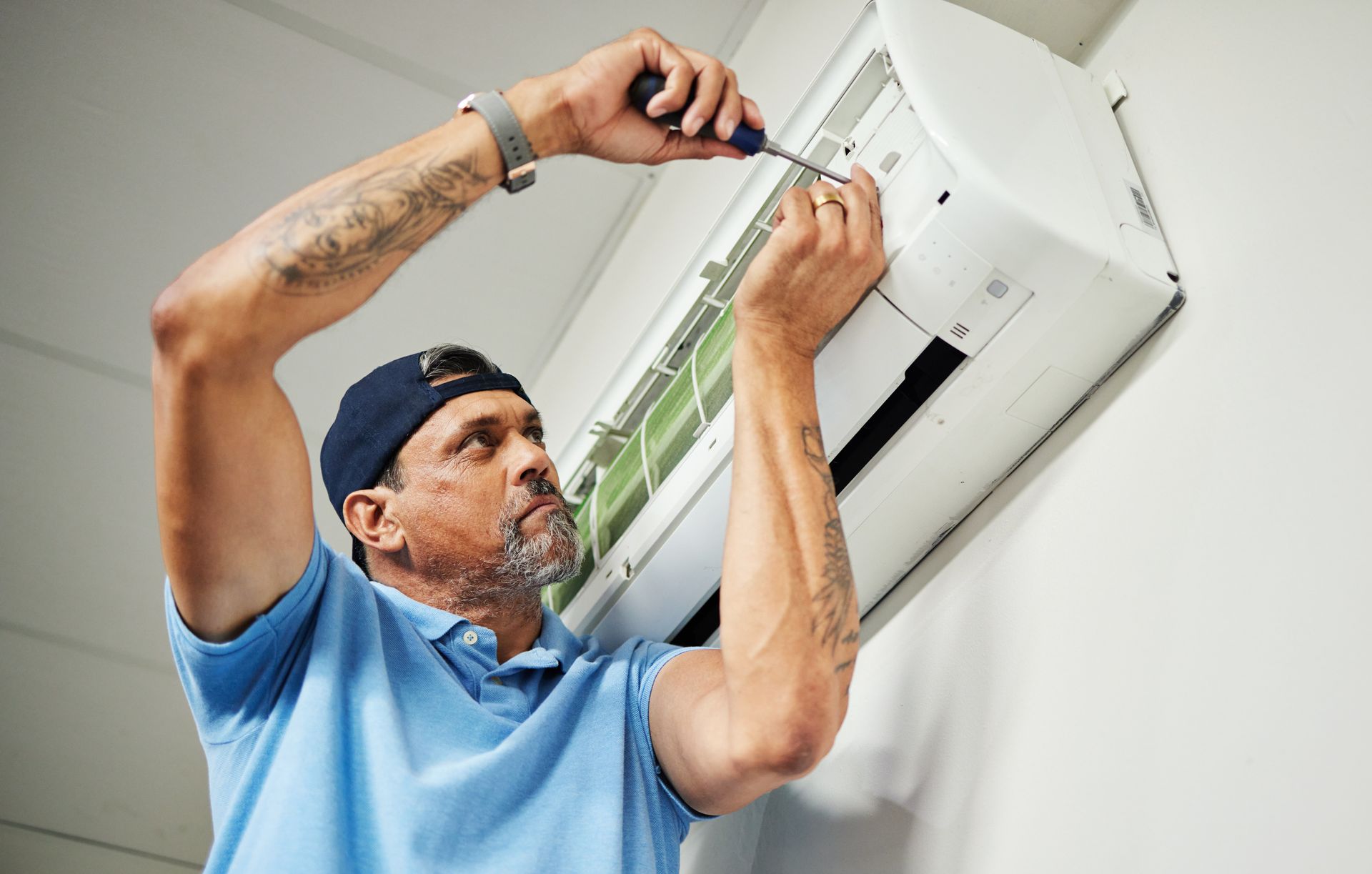 A person in blue shirt fixes an air conditioner with a screwdriver.