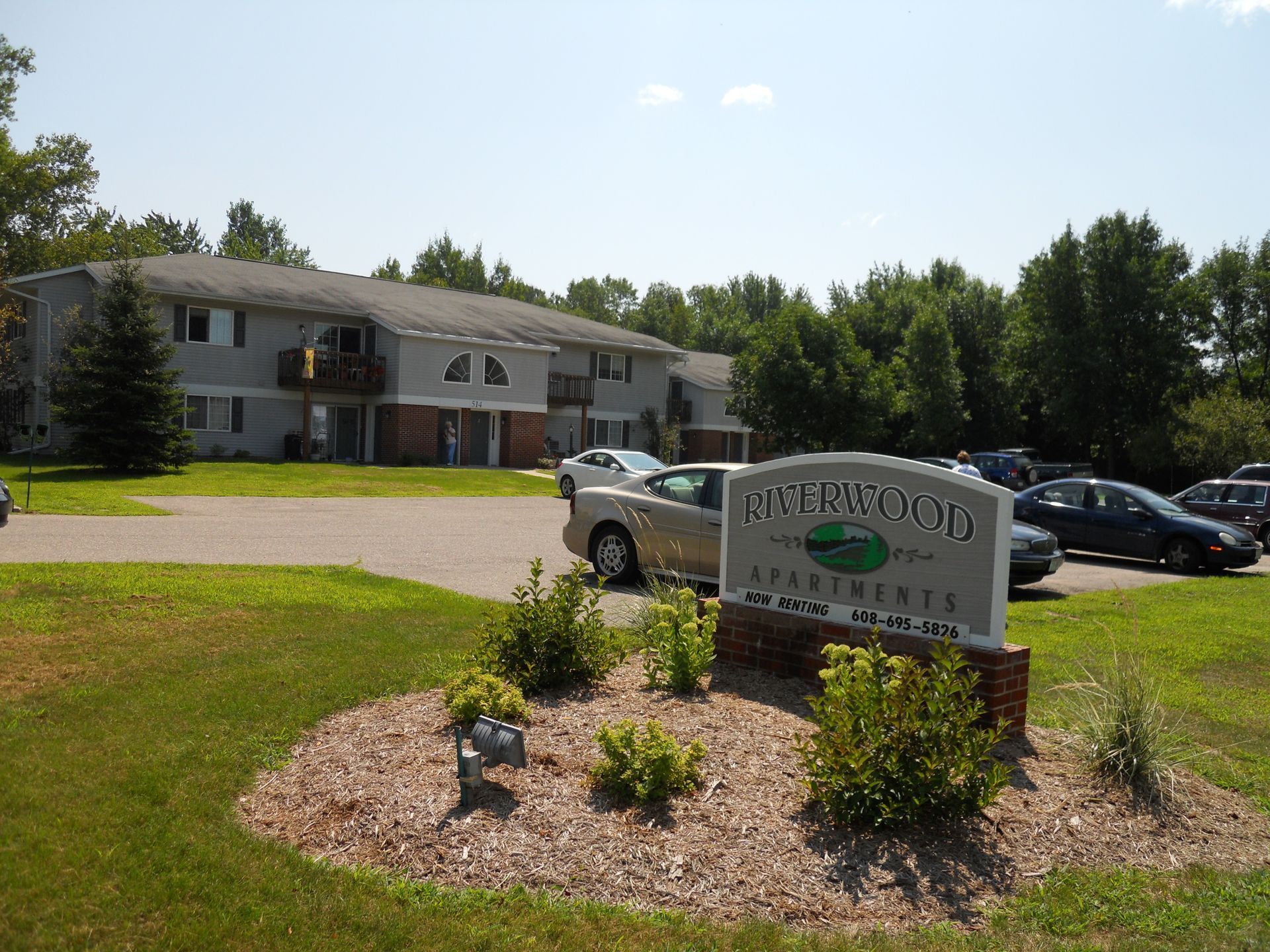 Office building with parking lot and sign reading “Hawthorn,” surrounded by trees and landscaping