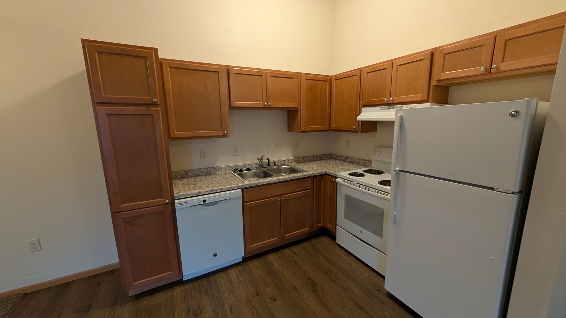 Small kitchen with wooden cabinets, white appliances, and a tiled countertop against beige walls.