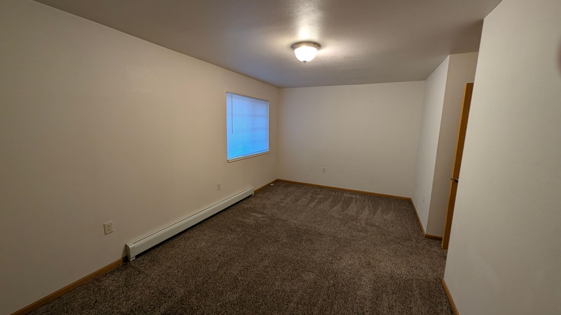 Empty carpeted room with white walls, a small window, and a ceiling light.