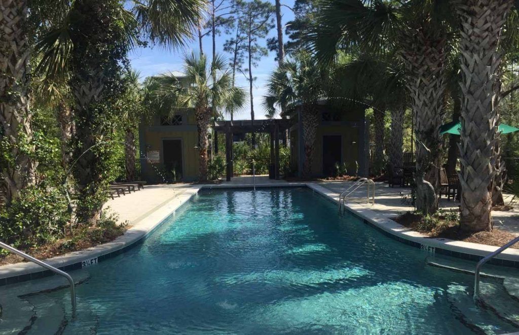 Swimming pool flanked by trees and small stone buildings under a wooden pergola.