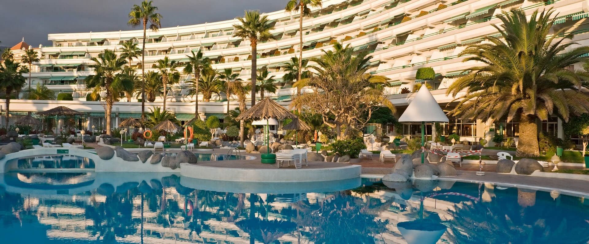 Swimming pool in front of a white building with palm trees.