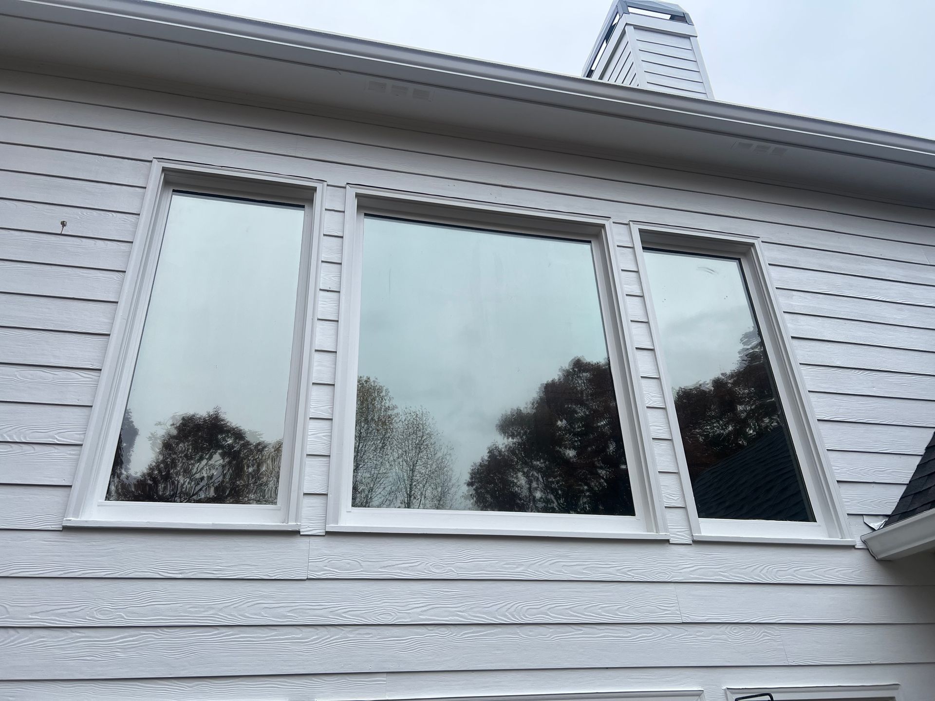 A white house with three windows and a chimney on the roof.