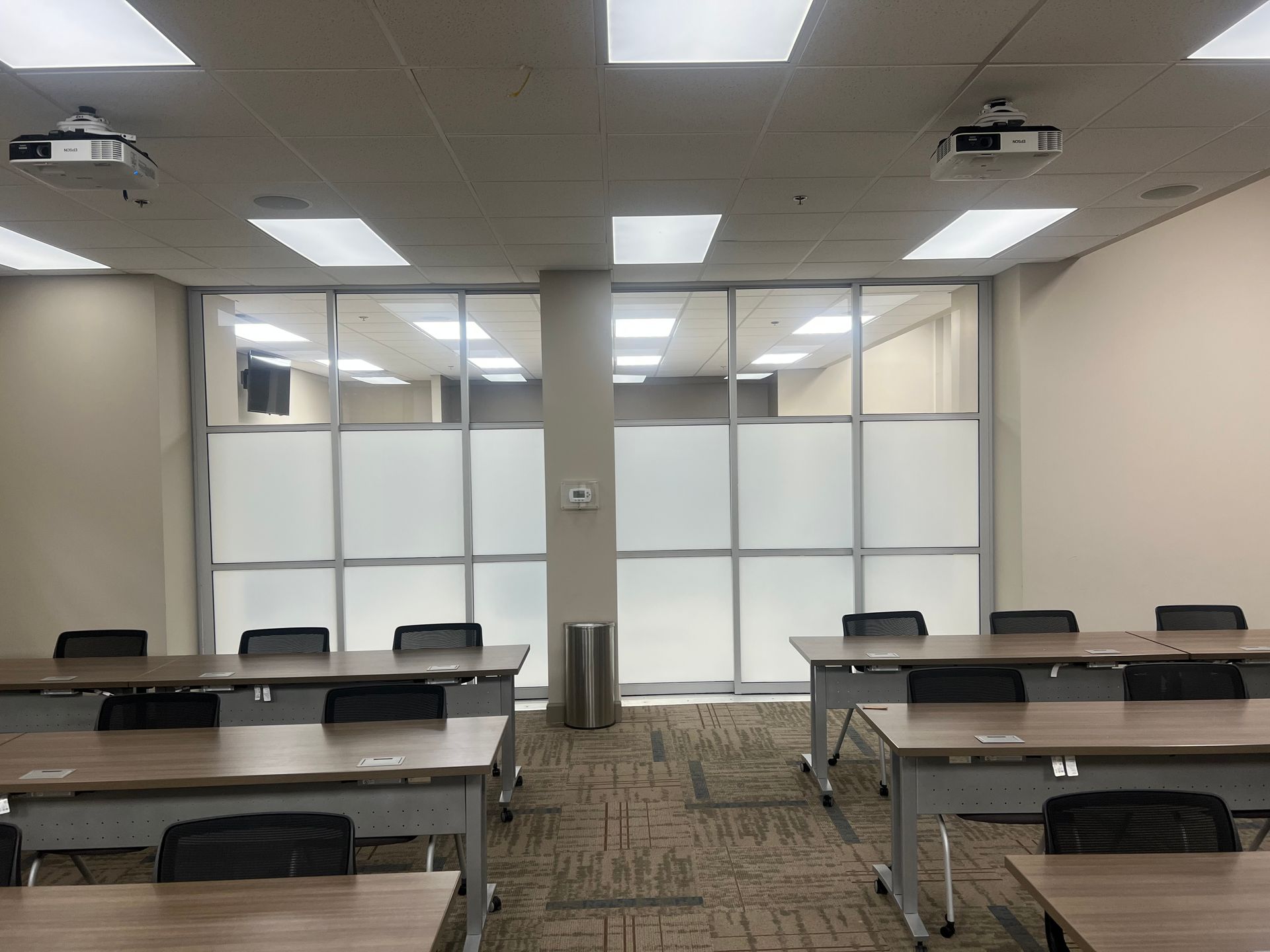 A classroom with tables and chairs and a projector on the ceiling.