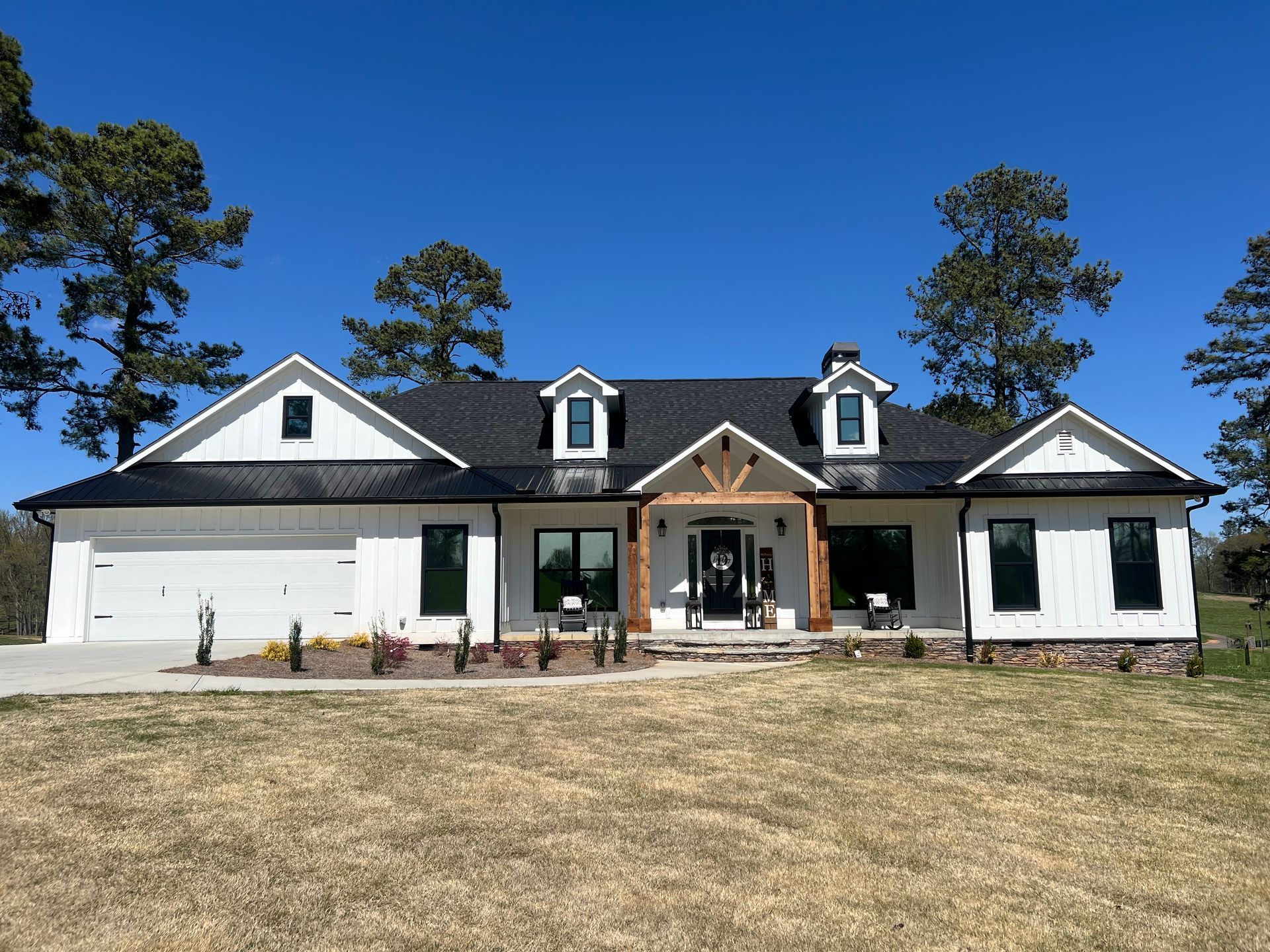 A large white house with a black roof is sitting in the middle of a grassy field.