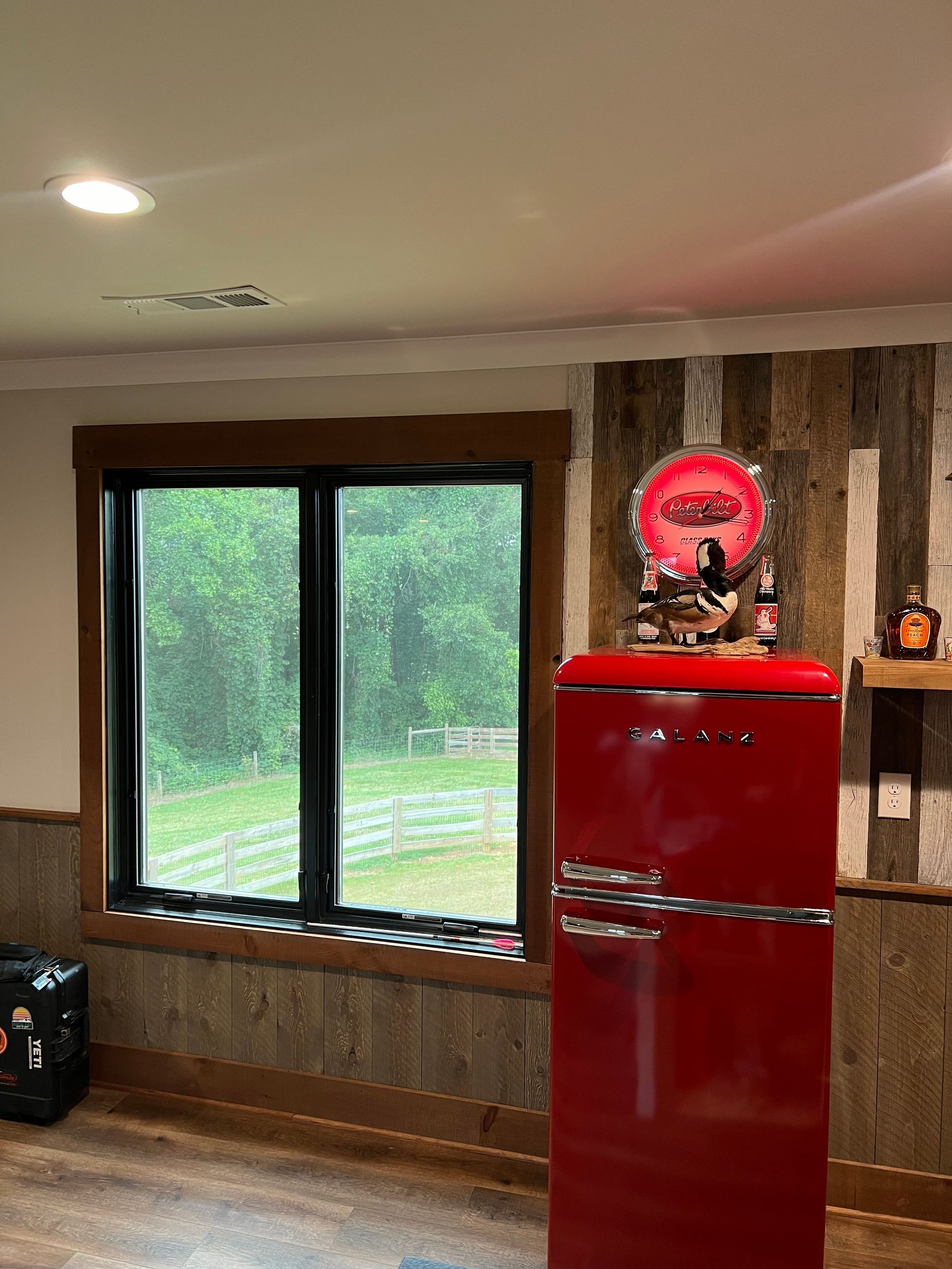 A red refrigerator is sitting in a room next to a window.