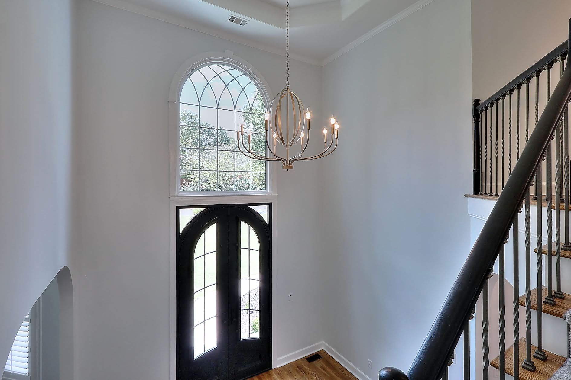 A hallway with a black door and stairs and a chandelier hanging from the ceiling.