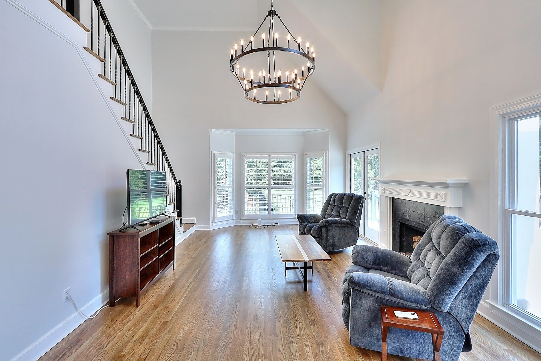 A living room with hardwood floors , a fireplace , two chairs , a television and a chandelier.