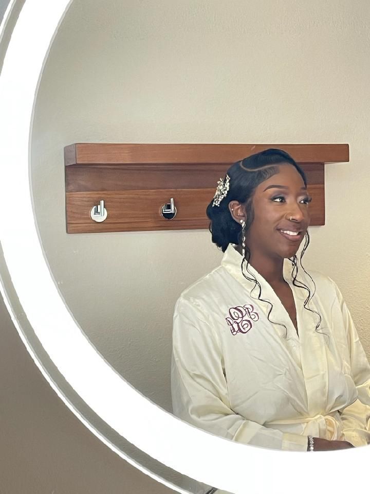 Woman in robe smiles in mirror; she wears elegant earrings and has her hair up.
