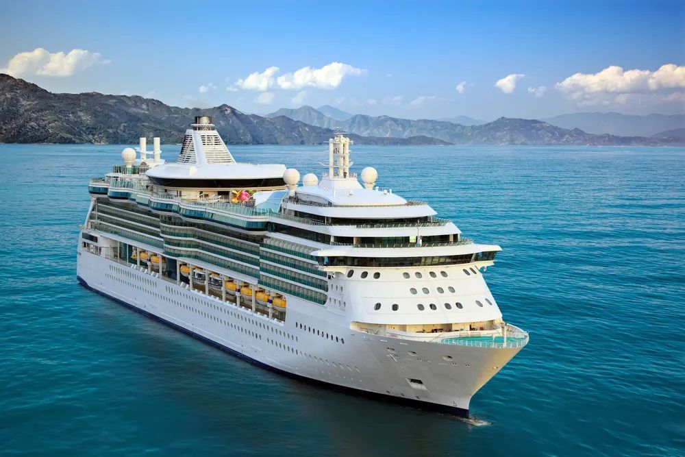 Cruise ship on blue water, mountains in the background, under a blue sky.