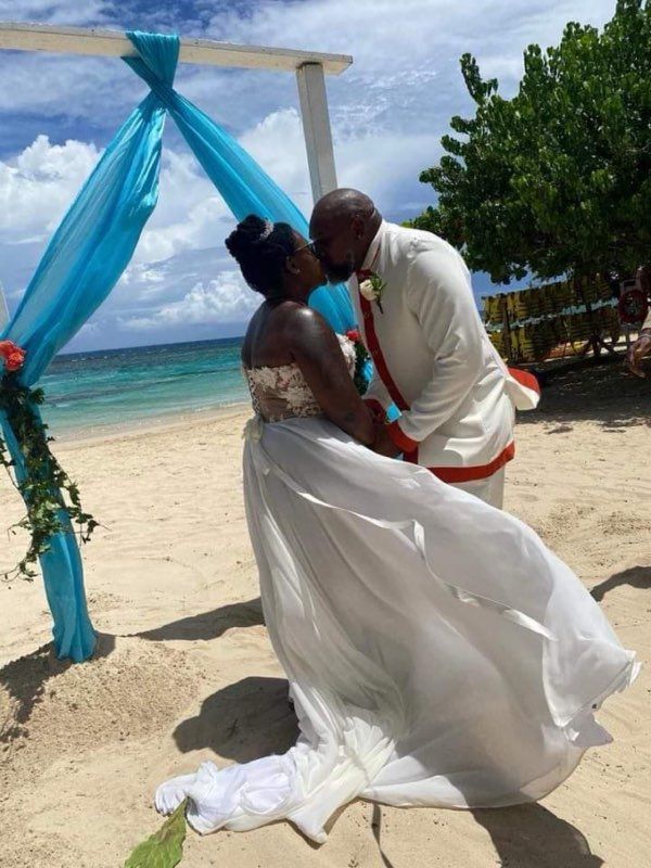 Bride and groom kiss on a beach at their wedding. They embrace under an arch with blue fabric, with an ocean view.