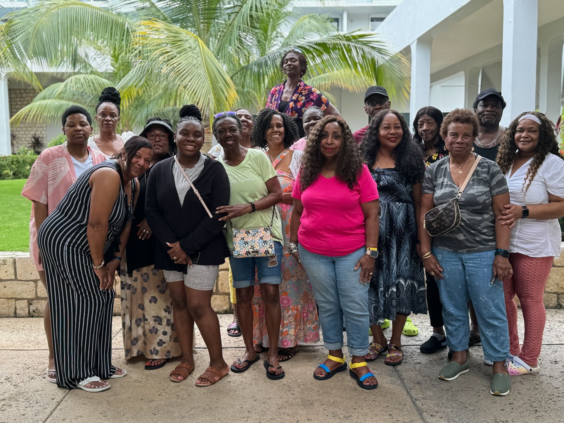 A group of people standing outdoors under palm trees, smiling and posing for a photo in front of a white building.