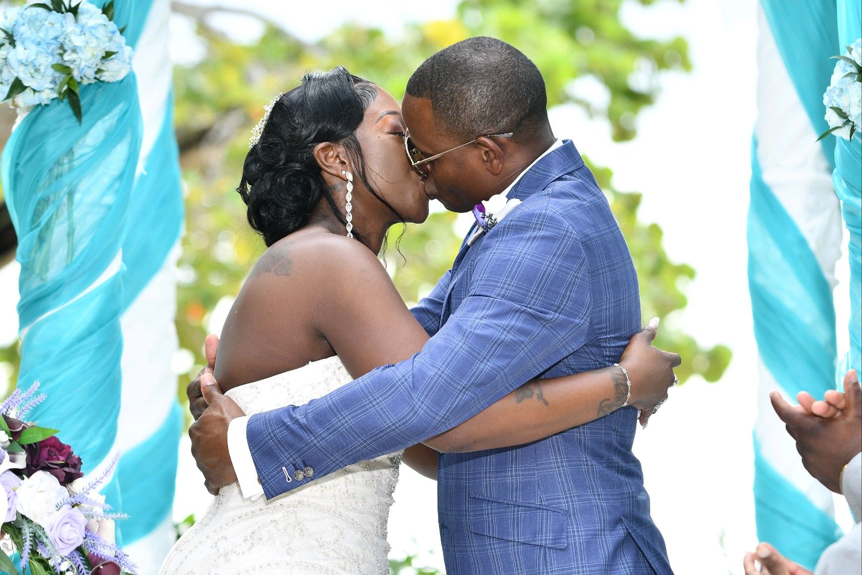 Newlywed couple kissing under turquoise archway at outdoor wedding.