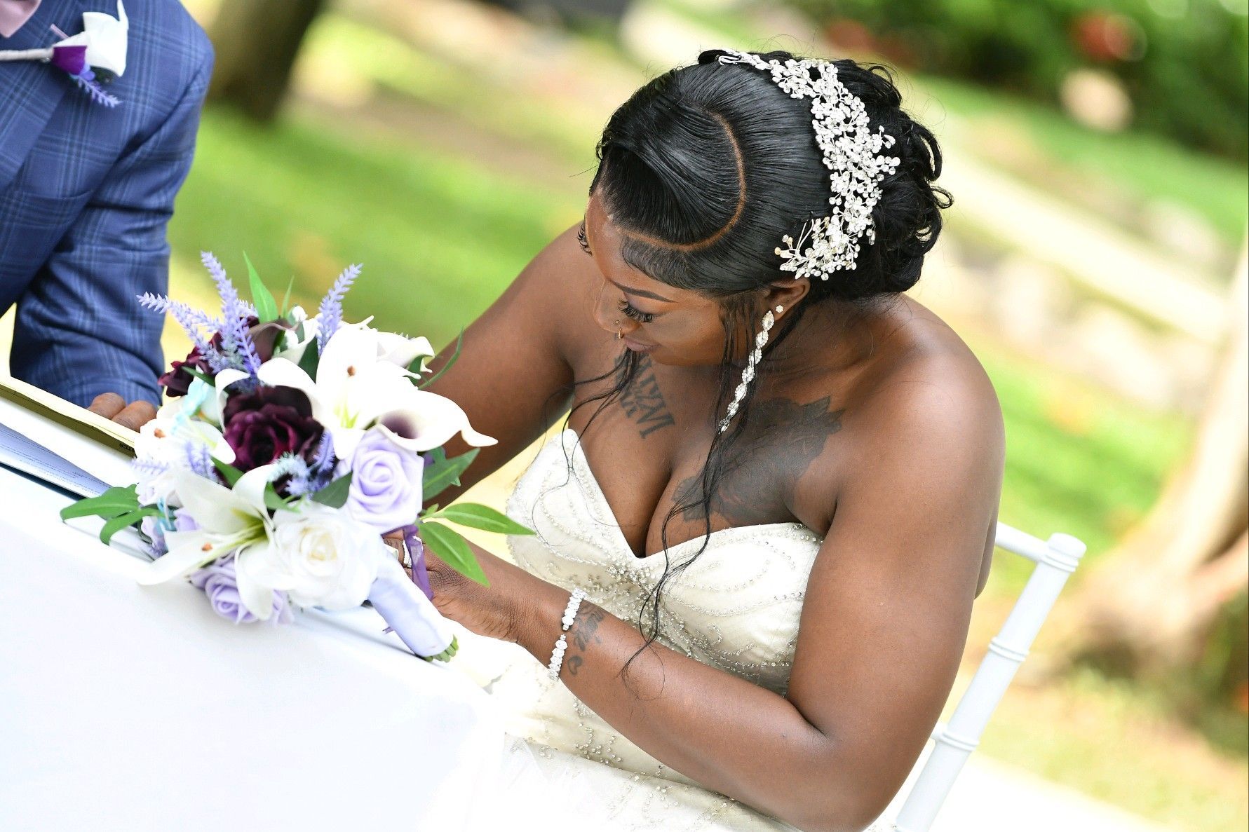 Bride in strapless wedding dress with a bouquet, signing a document outdoors.