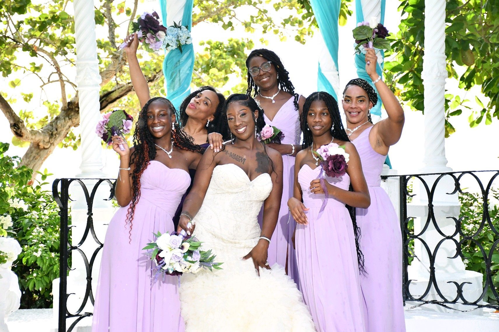 Bride and bridesmaids in lavender dresses pose outdoors.