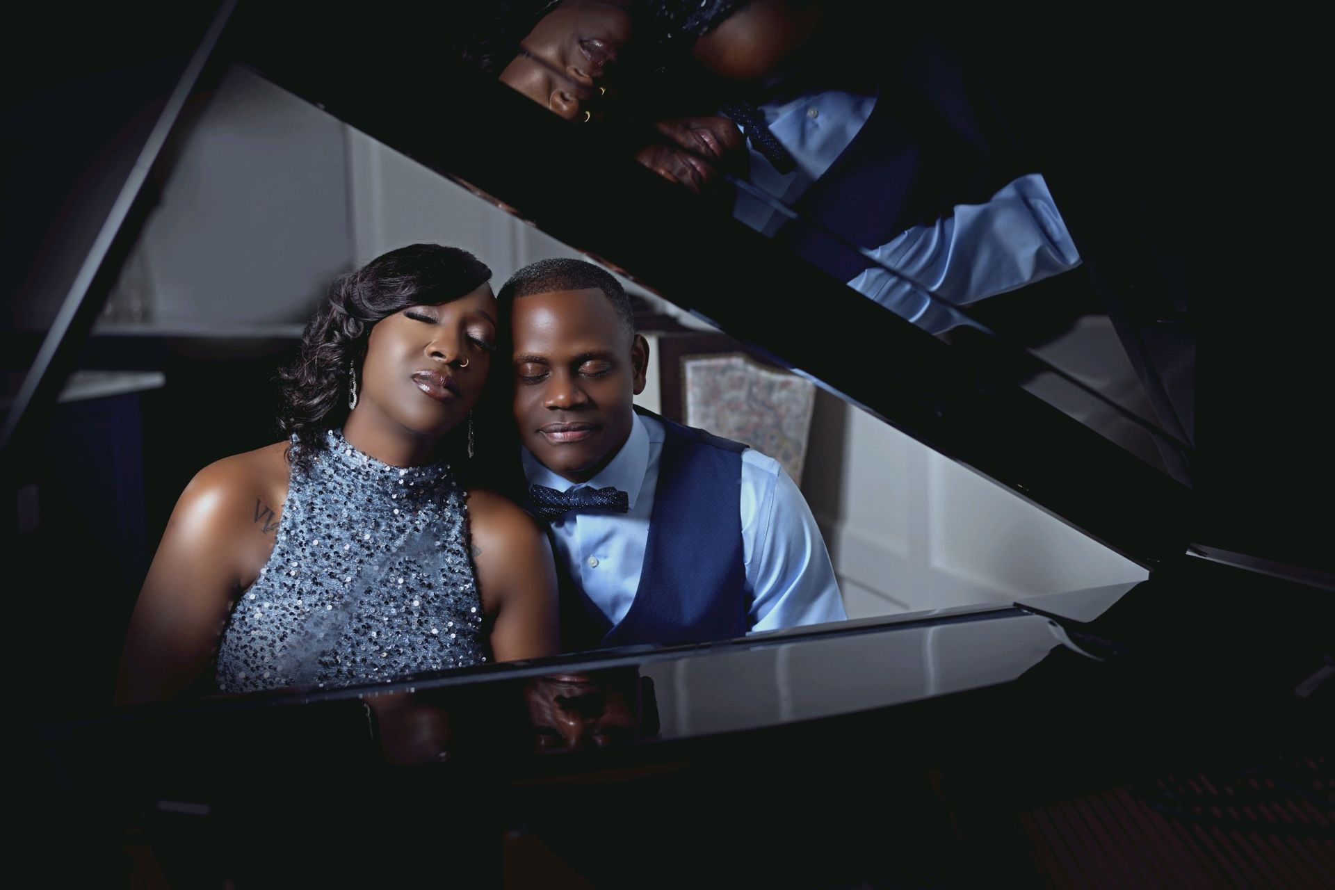 Couple seated at a grand piano, gazing at each other. Woman in a beaded dress, man in a vest and bow tie.