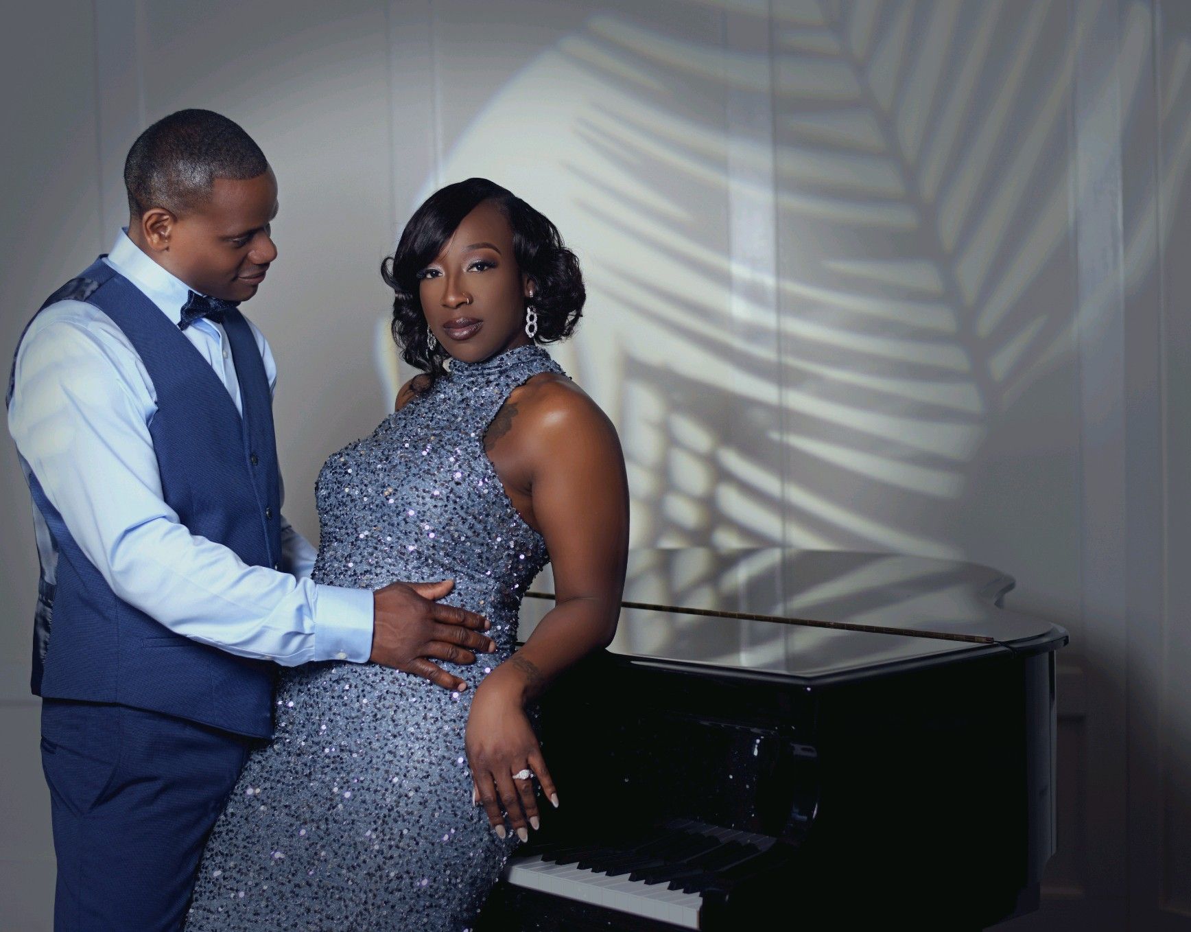 Man in blue vest and woman in sequin dress by a piano. Soft shadows.
