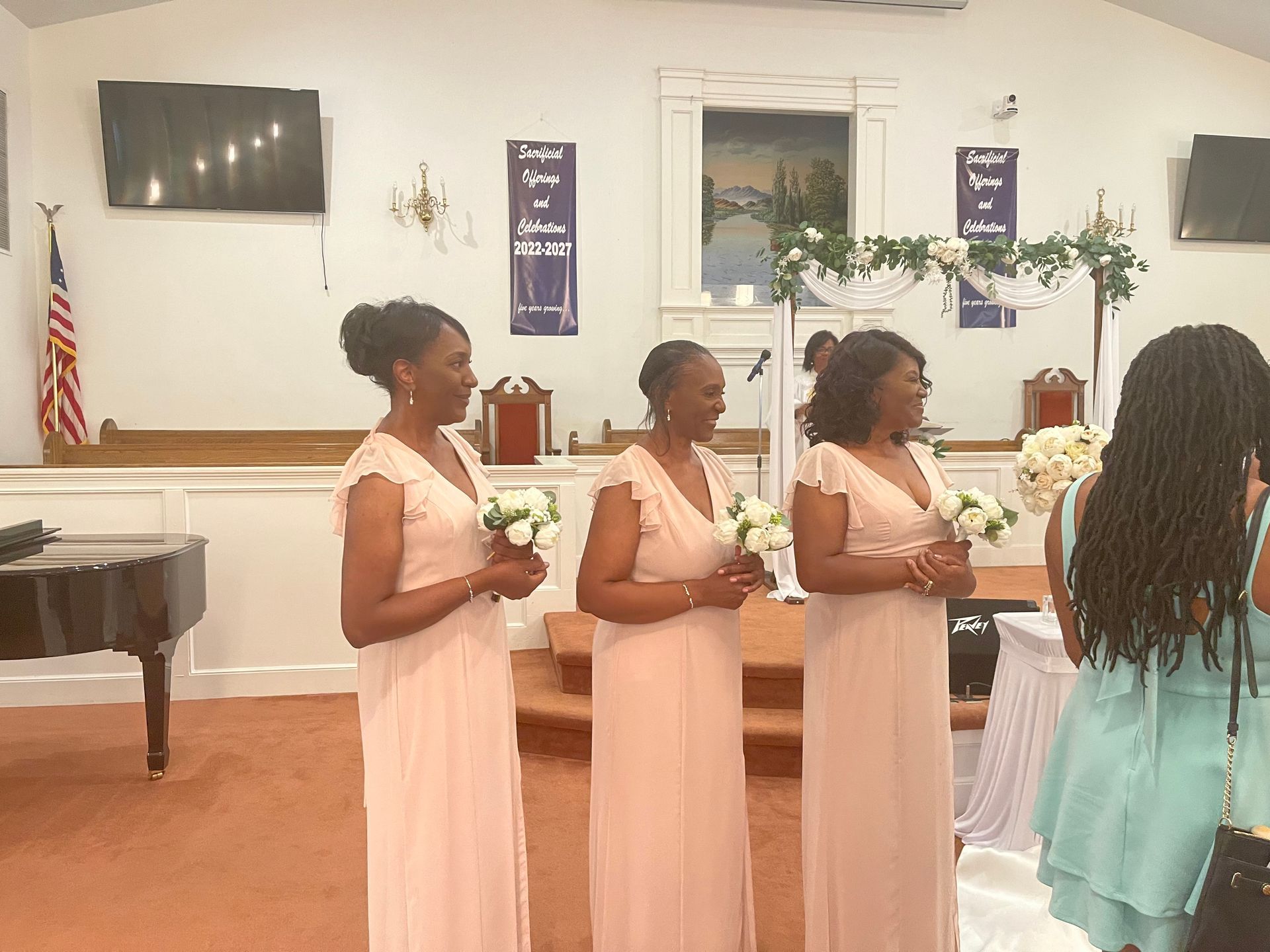 Bridesmaids in pink dresses holding bouquets, standing at a church alter.