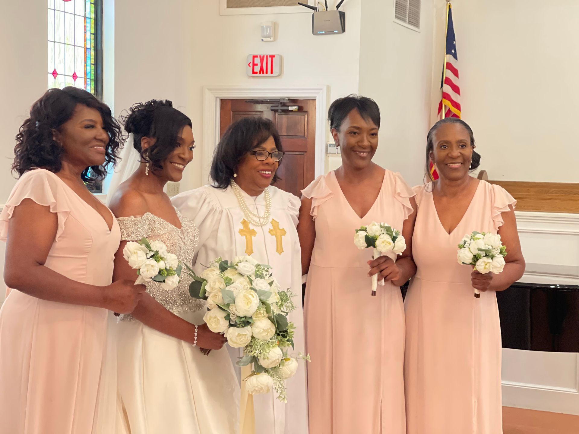 Wedding party in a church. Bride and bridesmaids in pink dresses with bouquets. Officiant in white.