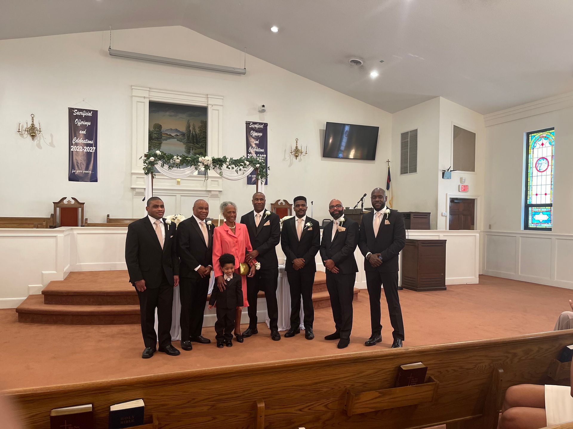 A wedding party poses inside a church. Men in suits stand with a woman and child on the altar.
