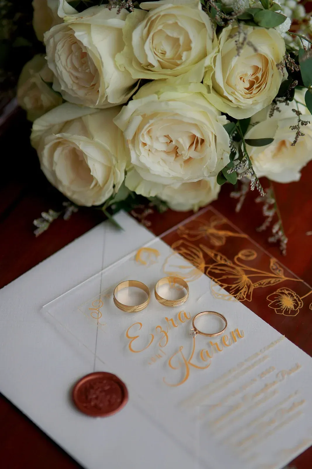 A couple of wedding rings sitting on top of a wedding invitation next to a bouquet of white roses.