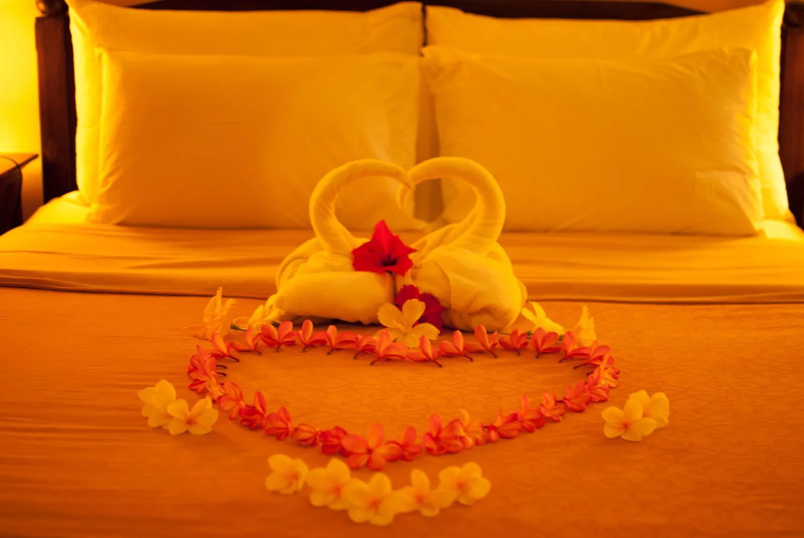 Bed decorated with towel swans, heart of flower petals.
