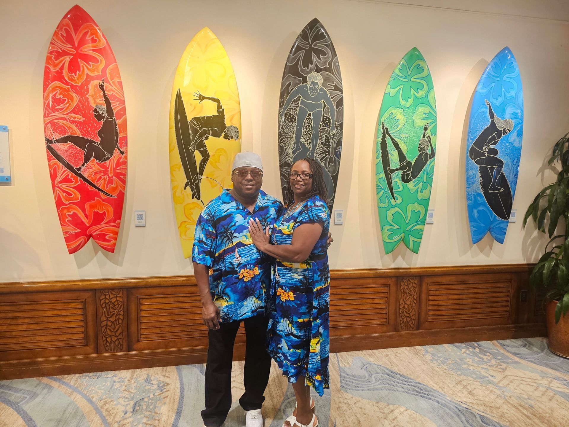 Two people posing in matching blue outfits in front of colorful surfboard wall art